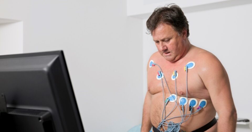 A man with an ECG hooked up to his chest is looking down at a monitor.